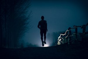 A man running on a dirty road during the night near a river in the country